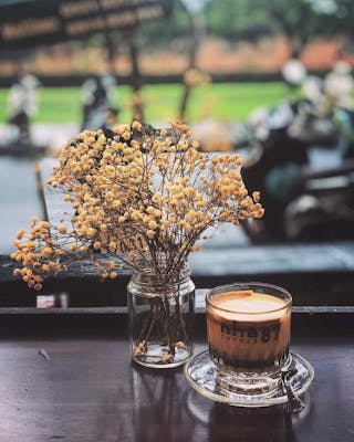 Tách cà phê và bình hoa trang trí trên bàn của quán Nhà 87 Coffee.